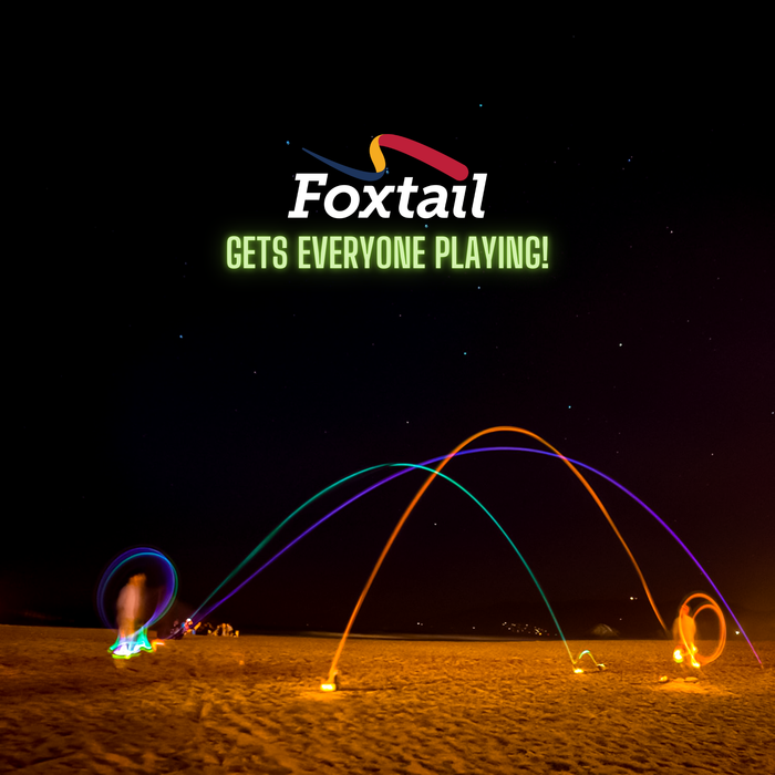 A nighttime beach scene shows glowing trails from a Foxtail LED tossed in motion, people enjoying this fun outdoor game, with the text “Foxtail LED Gets Everyone Playing!” displayed in white and green above.
